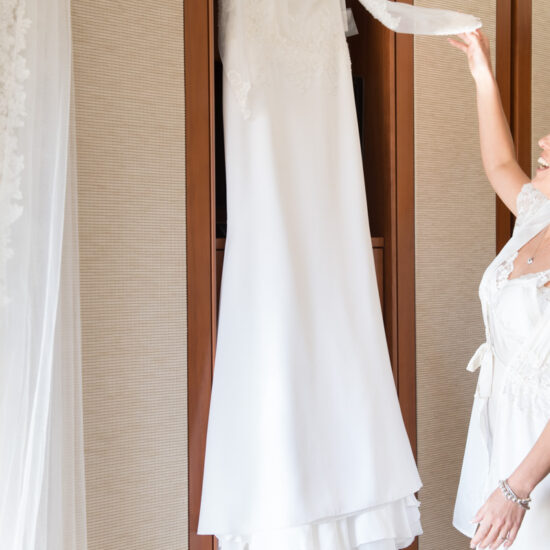 Matrimoni, sposa che ammira il vestito appeso davanti l'armadio in camera prima d'indossarlo