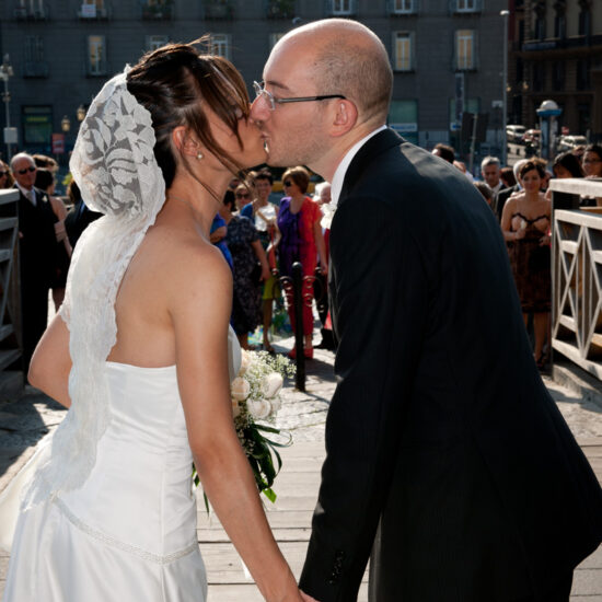 Matrimoni, bacio di sposi all'uscita del municipio visto dalle loro spalle e con gli invitati dietro