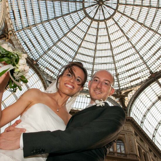 Matrimoni, sposi abbracciati visti dal basso con la cupola della galleria umberto in alto sopra di loro, lei ha il bouquet in mano