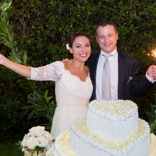 Matrimoni, sposi che agitano stelline filanti davanti alla torta nunziale bianca a forma di cuore, sorridono e mi guardano