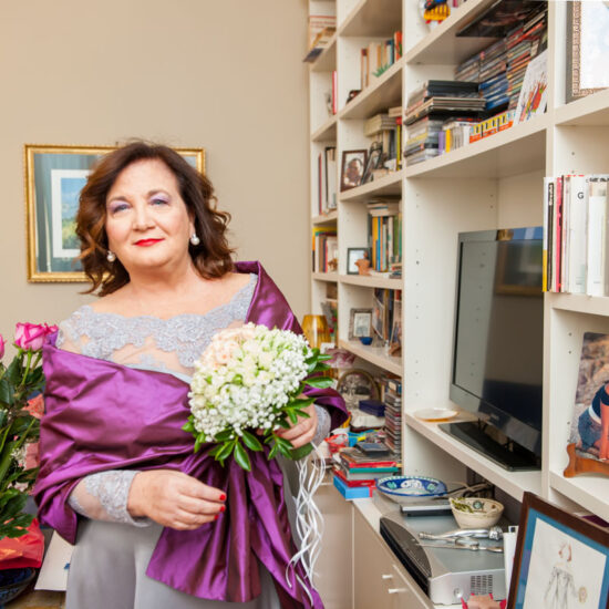 Matrimoni, sposa con bouquet in mano viene verso il fotografo camminando affianco alla libreria piena di libri e una foto che la ritrae da ragazza