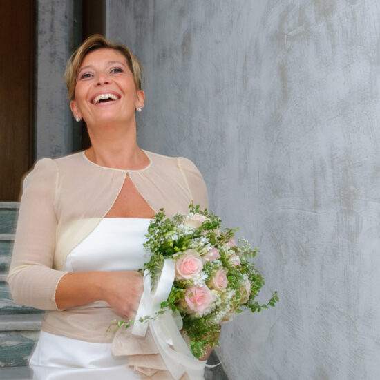 Matrimoni, sposa sorridente mentre scende le scale con bouquet