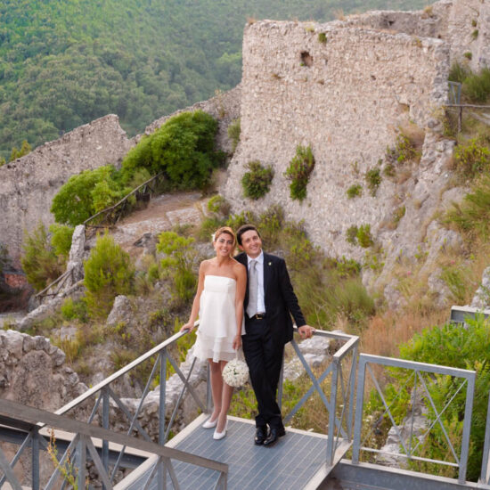 Matrimoni, sposi appoggiati alla ringhiera di una passerella all'esterno delle mura del castello di arechi, inquadratura dall'alto, bosco in fondo