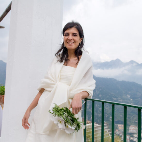 Matrimoni, sposa appoggiata alla ringhiera affianco ad una colonna bianca con un paesaggio di valli al di sotto