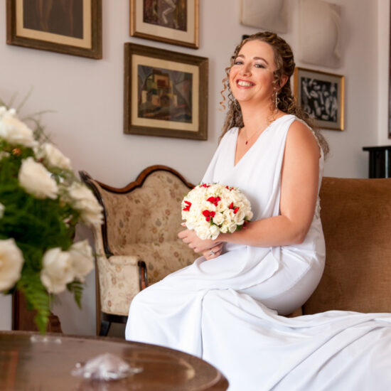 Matrimoni, sposa su divano con bouquet in mano, quadri alle spalle