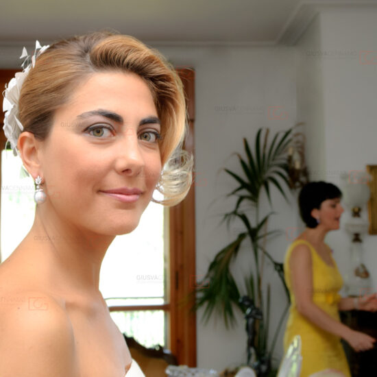 Matrimoni, la sposa in primo piano guarda in macchina mentre si stra preparando i capelli a casa prima di vestirsi