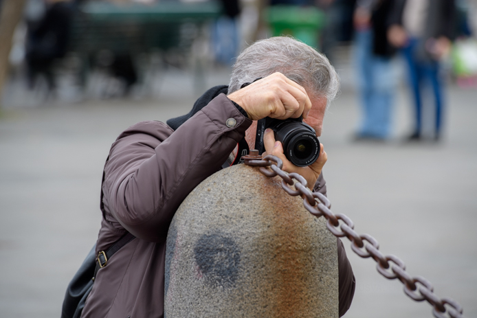 modulo base del corso di fotografia, uomo che scatta appoggiato ad un pilone dal quale fuoriesce una catena