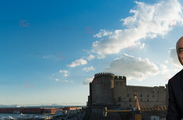 Ritratto panoramico a professionista contabile sorridente in giacca blu e camicia bianca con sfondo del castello Angioino, porto e golfo di Napoli