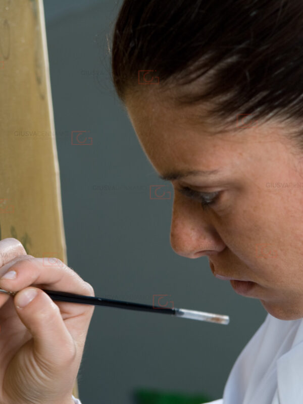 Ritratto di profilo a restauratrice professionista intenta ad operare su di una tela dipinta.